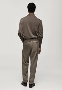 Pull en tricot marron avec un col, associé à un pantalon beige clair. La tenue présente une coupe décontractée et un design minimaliste.