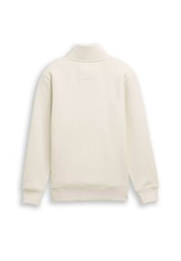 Sudadera de color crema con un cuello alto, que cuenta con mangas largas y un detalle de parche cuadrado en la parte posterior. Textura suave y diseño minimalista.
