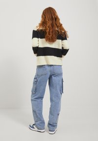 Pullover aus Wollmischung mit schwarzen und cremefarbigen horizontalen Streifen; kombiniert mit hellblauen Cargo-Jeans mit Seitentaschen und einer entspannten Passform.