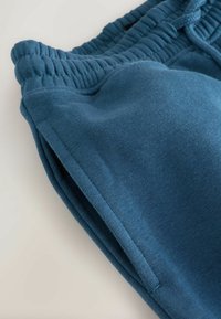 Teal bomullsbyxor i sweat material har ett rynkat midjeband, dragsko och sidofickor. Tyget har en mjuk textur med en något borstad yta.