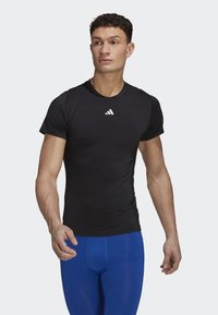 Camiseta deportiva negra de manga corta, con un pequeño logo blanco en el pecho. Combinada con leggins ajustados azules, que destacan un ajuste aerodinámico.