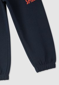 Granatowe joggery wykonane z miękkiego materiału, z elastycznymi mankietami i słowem "SPIDER" w jaskrawoczerwonym kolorze z przodu.