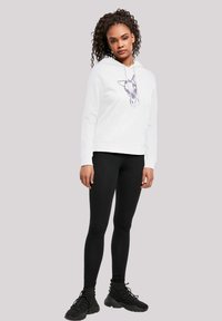 Hvit hettegenser med grafikk av et dyrehode, frontlomme, kombinert med svarte leggings og svarte joggesko. Glatt stofftekstur.
