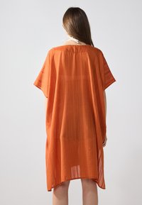 Túnica ligera naranja con un corte holgado, mangas cortas y una sutil textura a rayas, con un dobladillo redondeado y un diseño de espalda abierta.