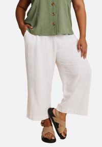 Vita linne byxor med vida ben och strukturerad yta, i kombination med en grön skjorta med knappar och beige sandaler med remmar.