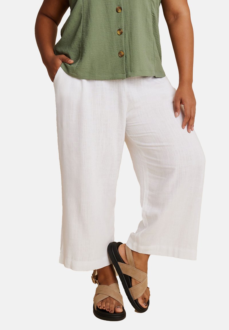 Vita linne byxor med vida ben och strukturerad yta, i kombination med en grön skjorta med knappar och beige sandaler med remmar.