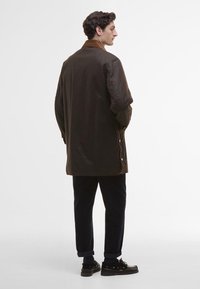 Barna külső kabát velúr gallérral, laza szabással, oldalán patentgombokkal, tengerészkék nadrággal viselve. Sima textúra és térd követő fazon.