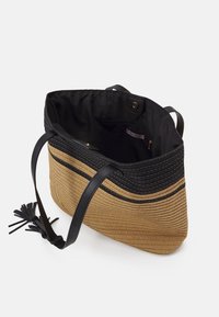 Sac fourre-tout en paille tressée marron avec des accents noirs, présentant une surface texturée, deux anses noires et un intérieur ouvert avec un doublage contrasté.