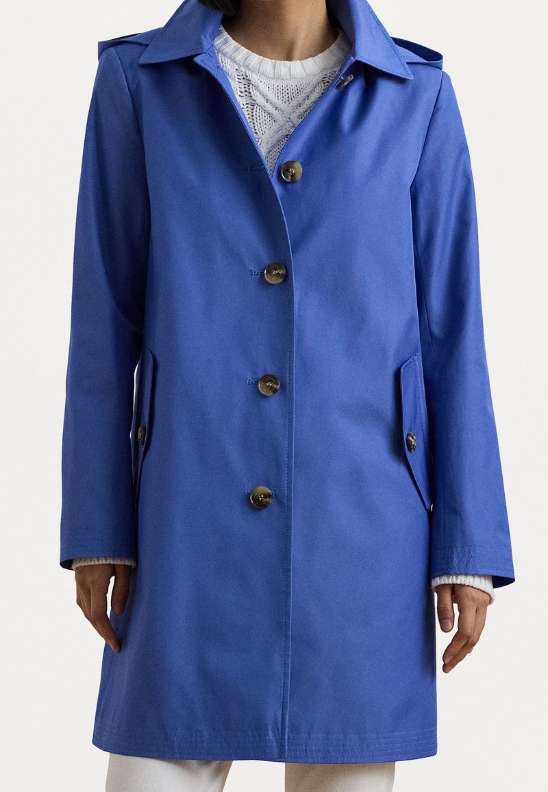 Impermeable azul con cuello con muesca, cinco botones grandes, bolsillos laterales y corte recto. Textura lisa y tela ligera.