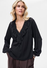 Czarna bluzka z głębokim dekoltem w kształcie litery V i marszczonymi brzegami, zdobiona misternymi koralikami. Miękki materiał i długie rękawy z paskowanymi mankietami.