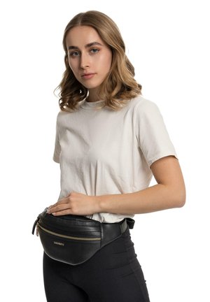 Marsupio in pelle nera con superficie texture, due cerniere e un accento dorato. Indossato in vita, abbinato a una camicia leggera e leggings.