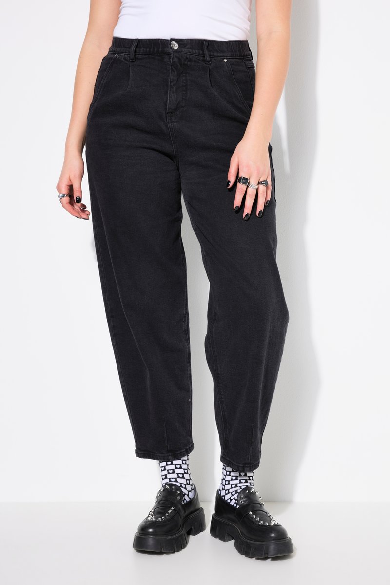 Donna che indossa pantaloni neri a vita alta e con taglio stretto, calzini bianchi con motivo, scarpe nere platform spesse, top bianco e anelli alle dita.