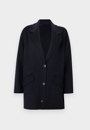 Temno modr plašč iz volnene mešanice z zarezanim ovratnikom, dvema sprednjima žepoma in tremi gumbi. Prevelik kroj z ravnimi rokavi.