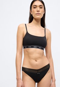 Braletă neagră din bumbac, cu bretele subțiri și bandă elastică cu logo. Bikini negri asortați, cu margine din dantelă și mic detaliu cu fundă la talie.