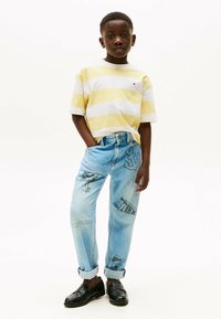 Gestreepte gele en witte katoenen t-shirt gecombineerd met licht gewassen spijkerbroeken met grafische borduursels. Zwarte instappers maken de outfit compleet.