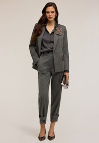 Harmaa pinstripe-puku, jossa on muotonsa mukainen bleiseri ja kapenevat housut, paritettu tummanharmaan paidan ja kukkakoristeen kanssa. Kiiltävä laukku.