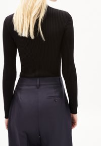 Haut noir à manches longues côtelé associé à un pantalon taille haute bleu marine avec un détail de bouton et une poche arrière. Design lisse et ajusté.