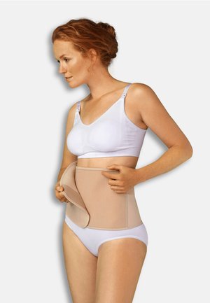 Beige buikondersteunende band met verstelbare banden, gladde textuur en zachte stof, gedragen over witte onderkleding.