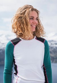 Sportovní triko s dlouhým rukávem v bílém těle, tyrkysovými rukávy a černými detaily, s růžovým prošíváním podél švů a ramen.