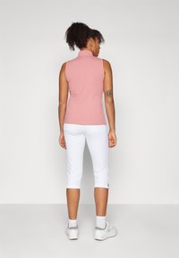 Top atlético sin mangas de color rosa con cuello alto, combinado con leggings cortos blancos que presentan aberturas laterales y una textura suave.