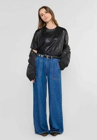 Top corto de cuero negro con mangas cortas, chaqueta oversized gris oscuro y jeans de mezclilla azul de pierna ancha con bolsillos frontales y un cinturón.