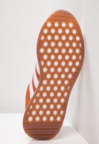 Gummisneakersula med ett geometriskt hexagonmönster i orange och vitt, med Adidas-logotyp på hälen.