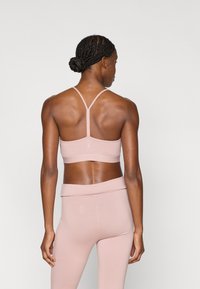 Αθλητικό σουτιέν ανοιχτό ροζ με λεπτές τιράντες, σχεδιασμό χωρίς ραφές και φαρδιά ταινία στο κάτω μέρος, σε συνδυασμό με ψηλόμεσα κολάν που ταιριάζουν.