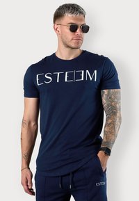 Navy blue short-sleeve t-shirt with white "ESTEEM" text. Cotton material, crew neck design, smooth texture, paired with matching joggers.