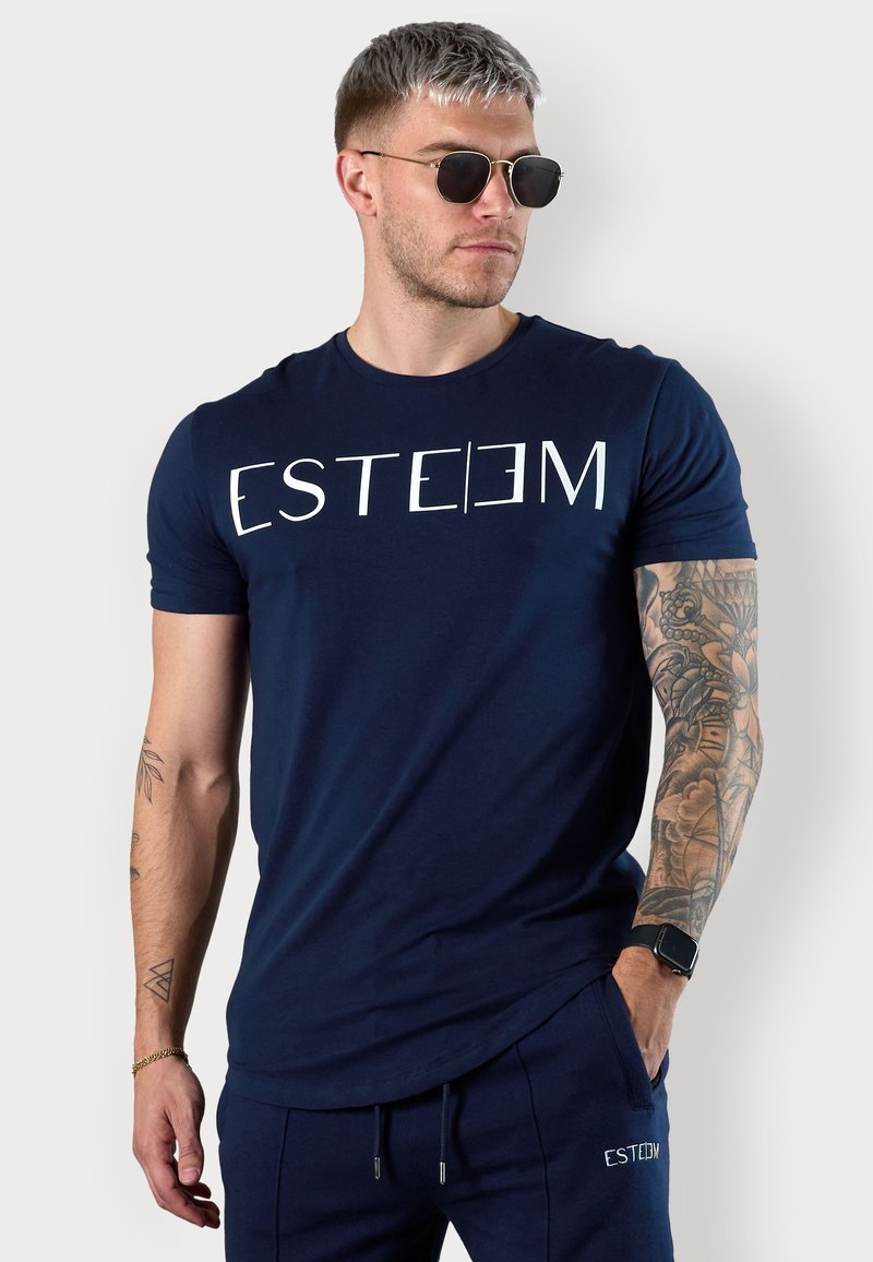 Navy blue short-sleeve t-shirt with white "ESTEEM" text. Cotton material, crew neck design, smooth texture, paired with matching joggers.