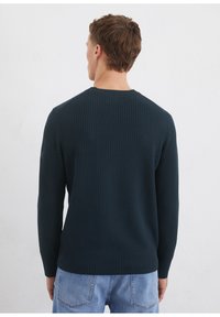 Dunkelgrüner, gerippter Pullover mit langen Ärmeln und rundem Halsausschnitt, der über einen strukturierten Stoff und eine taillierte Silhouette verfügt.