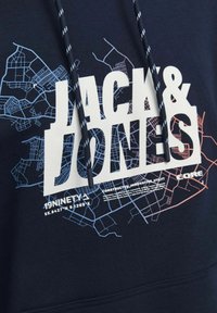 Sudadera azul marino con un gran gráfico blanco que incluye el texto "JACK & JONES", superpuesto con diseños abstractos de un mapa de la ciudad en azul y rojo. Capucha con cordón.