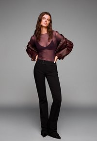 Genomskinlig, mörklila långärmad topp som matchas med högmidjade svarta byxor och en vinröd läderjacka, med vida ärmar och en elegant design.