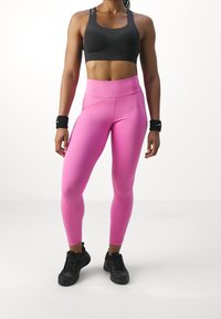 Svart sportbh med texturerad design, högmidjade rosa leggings med glansig finish, tillsammans med svarta träningsskor.