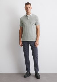 Koszulka polo w jasnozielonym kolorze z bawełny, krótki rękaw i zapięcie na trzy guziki; zestawiona z ciemnoniebieskimi spodniami slim-fit i czarnymi butami.