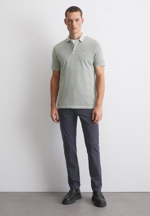 Polo shirt in lichtgroene katoen met korte mouwen en een drie-knopenrij; gecombineerd met donkerblauwe slim-fit broek en zwarte schoenen.