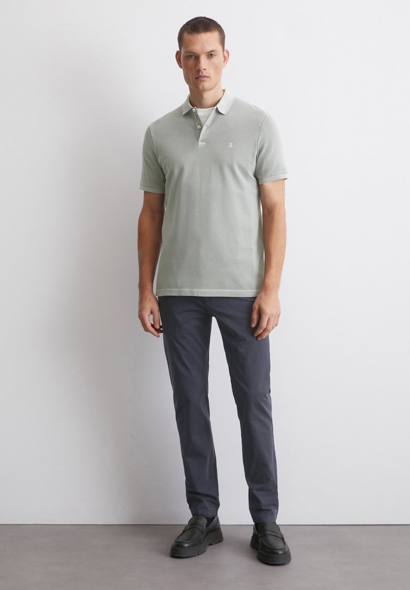 Koszulka polo w jasnozielonym kolorze z bawełny, krótki rękaw i zapięcie na trzy guziki; zestawiona z ciemnoniebieskimi spodniami slim-fit i czarnymi butami.