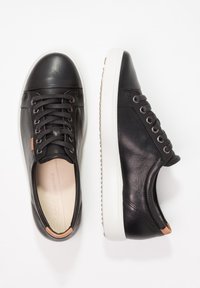 Par de zapatillas de cuero negro con suelas blancas y cordones negros, mostradas desde vistas superior y lateral sobre un fondo blanco.