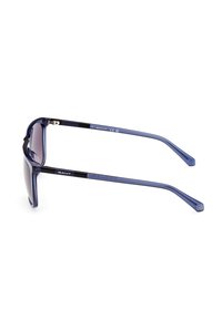 Gafas de sol con montura azul transparente y lentes degradados. Presentan un acento en las patillas de color negro con branding. Textura suave y diseño elegante.