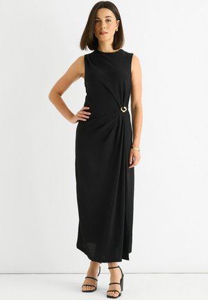 Black sleeveless maxi dress with a twisted front detail, accented by a gold clasp. Smooth fabric with a relaxed fit and side slit.