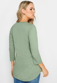 Långärmad, ljusgrön topp med rundad nederkant och mjukt, texturerat tyg. Har en rundad halsringning och en avslappnad passform.