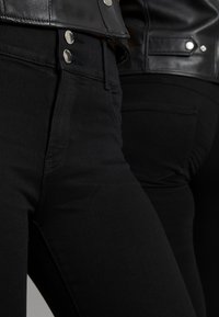 Calças skinny de denim preto com detalhes em metal prateado. Design ajustado, textura suave e uma linha de cintura limpa e plana.