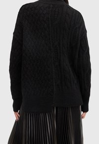 Pull noir en maille avec motifs torsadés, encolure côtelée et fentes latérales. Texture douce, coupe décontractée et détails texturés.