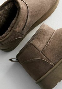 Bottines en daim marron avec doublure douce, bout arrondi et semelle texturée. Caractéristiques d'un cuir supérieur cousu et d'une languette pour un enfilage facile.