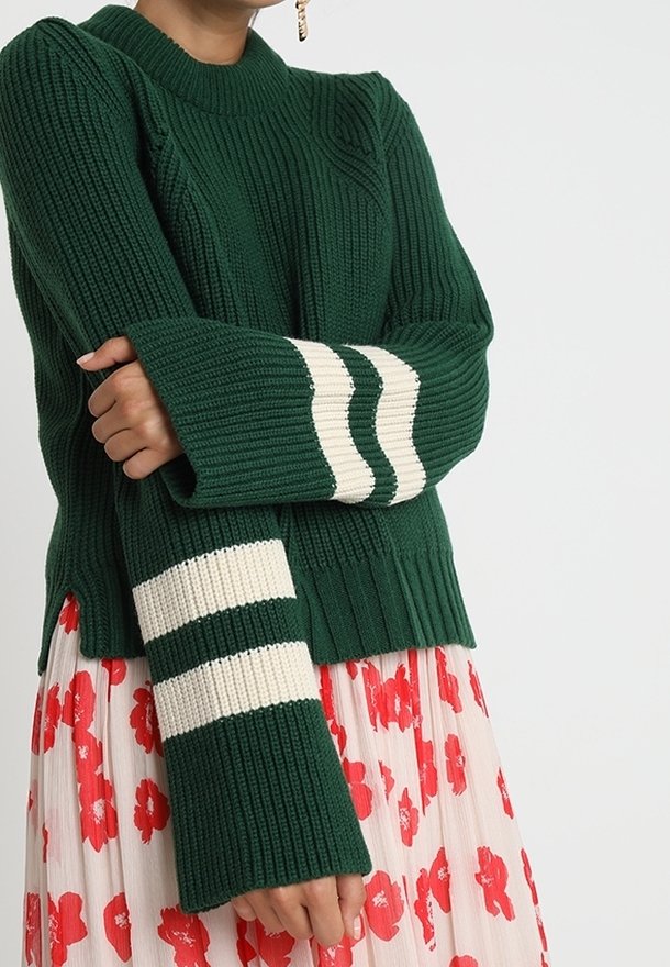 Maglione verde lavorato a maglia con una texture a coste, caratterizzato da maniche lunghe con strisce crema e un collo alto, abbinato a una gonna floreale.