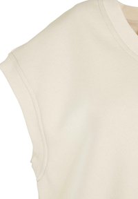 Haut en maille beige sans manches avec col en V côtelé et bords aux emmanchures, laissant apparaître le haut de la poitrine et des épaules.