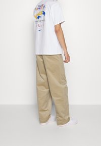 Vit t-shirt med kort ärm som har en färgglad grafisk design på ryggen, tillsammans med lösa beiga cargobyxor och vita sneakers.