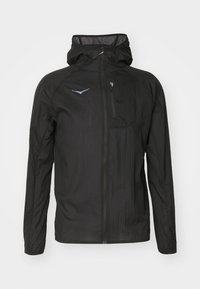 Veste légère noire en tissu texturé, avec une fermeture éclair sur le devant, une capuche et une petite poche poitrine avec un accent de logo.