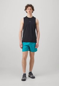 Camisa de alças preta e calções desportivos teal, complementados por ténis cinzentos. Design minimalista com logótipos subtils.