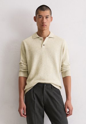Hellgelbe Strickjacke mit Polo-Kragen, zwei Knöpfen und gerippten Manschetten, kombiniert mit anthrazitfarbenen, taillierten Hosen.
