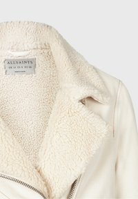 Giacca color crema foderata in shearling con un ampio colletto, dotata di una cerniera metallica e un tessuto esterno testurizzato. Etichetta visibile all'interno.